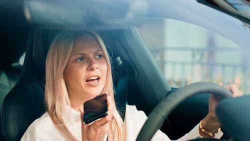 woman holding smartphone while seated behind steering wheel in vehicle