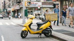 delivery scooter with cargo box and helmet parked on busy urban street corner