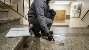 gloved inspector pointing at cracked wet floor tile near building staircase with notebook